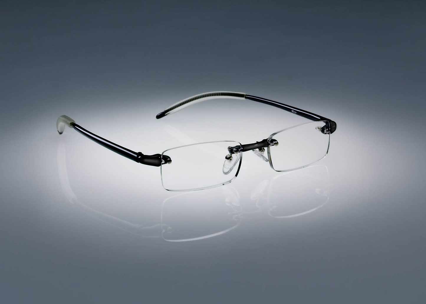 A pair of black colored Ultimate Reading Glasses resting on a table, illuminated by a soft spotlight.