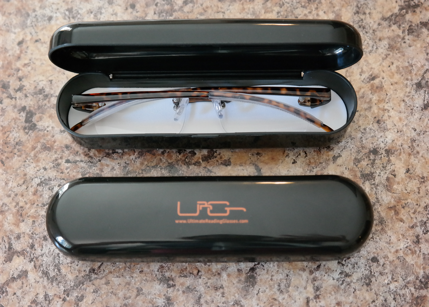 The Black Ultimate Reading Glasses hard case with tortoise reading glasses inside, resting on a table.