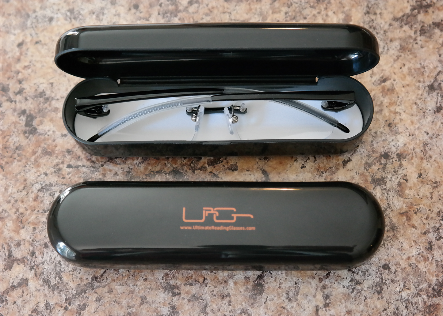 The Black Ultimate Reading Glasses hard case with black reading glasses inside, resting on a table.