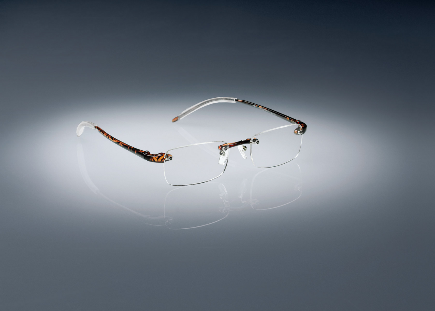 A pair of tortoise colored Ultimate Reading Glasses resting on a table, illuminated by a soft spotlight.