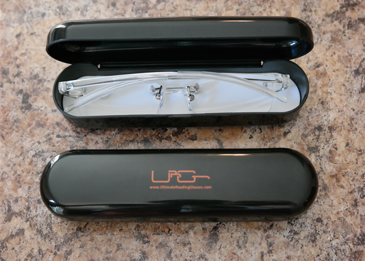 The Black Ultimate Reading Glasses hard case with clear reading glasses inside, resting on a table.