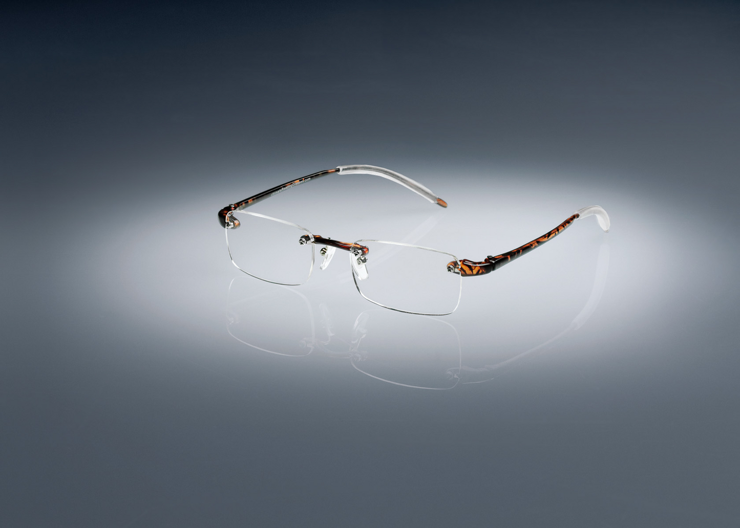 A pair of tortoise colored Ultimate Reading Glasses resting on a table, illuminated by a soft spotlight.