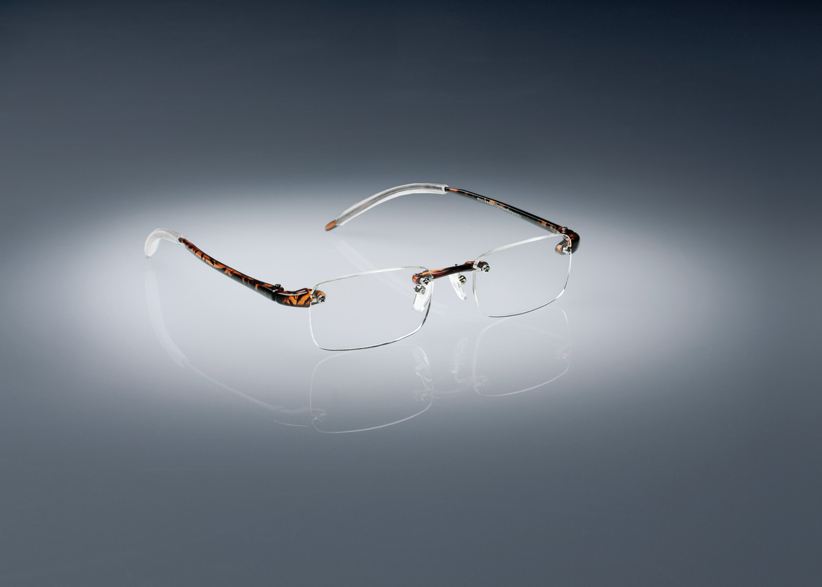 A pair of tortoise colored Ultimate Reading Glasses resting on a table, illuminated by a soft spotlight.